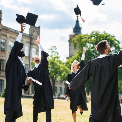 young graduated students throwing up graduation caps in university garden